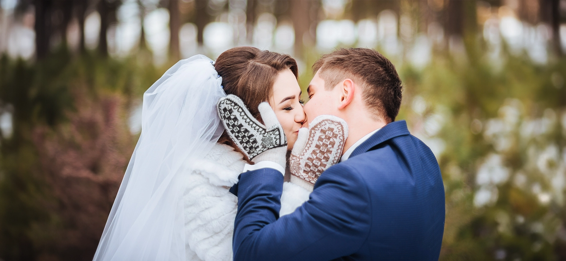 Couple de mariés s'embrassant en extérieur lors d'un mariage d'hiver, portant des moufles chaudes.